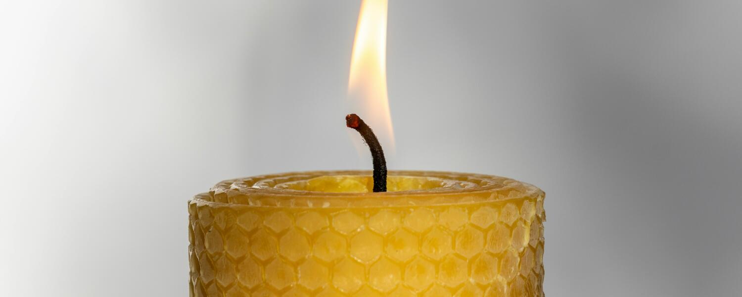 lit beeswax candle on a grey background