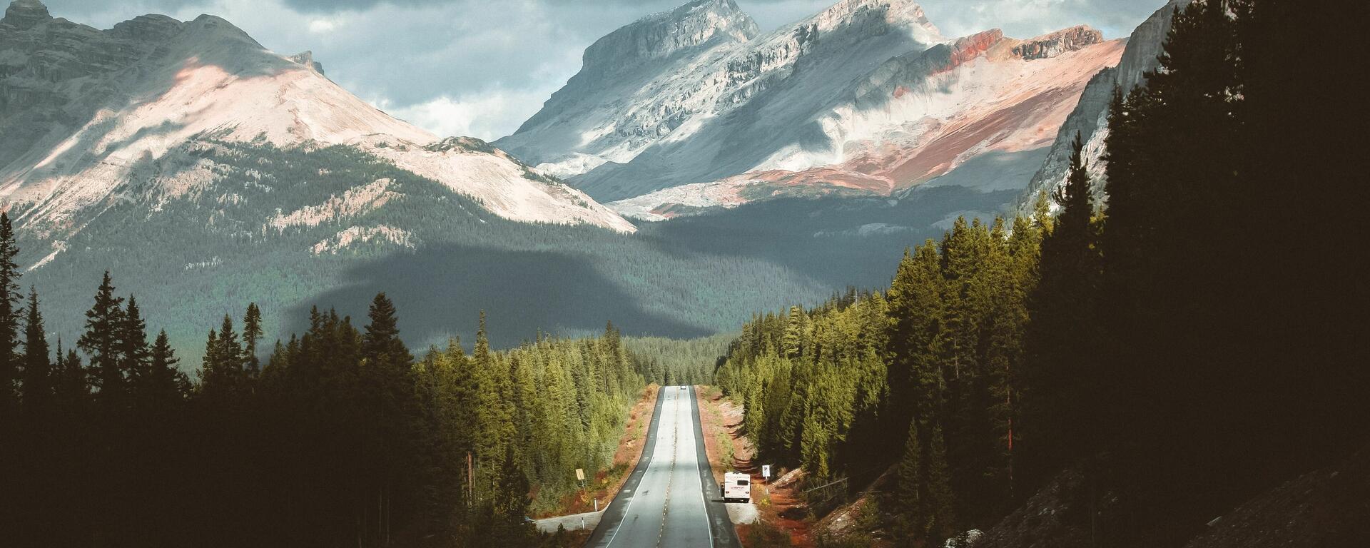 Gray concrete road between green trees and mountains during daytime