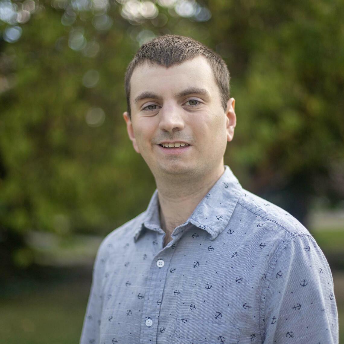 Man in a blue button down looks at the camera and smiles