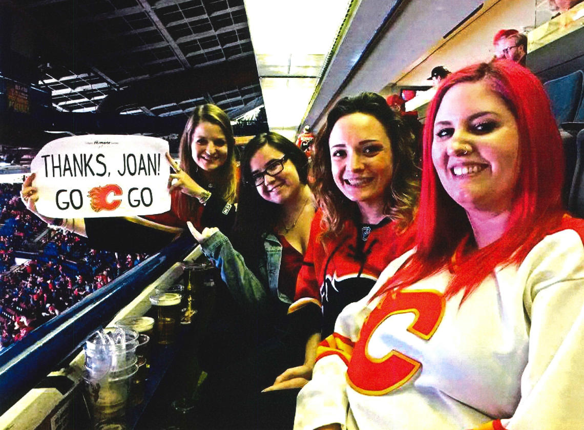 Four women at a hockey game holding a sign that says: Thanks, Joan