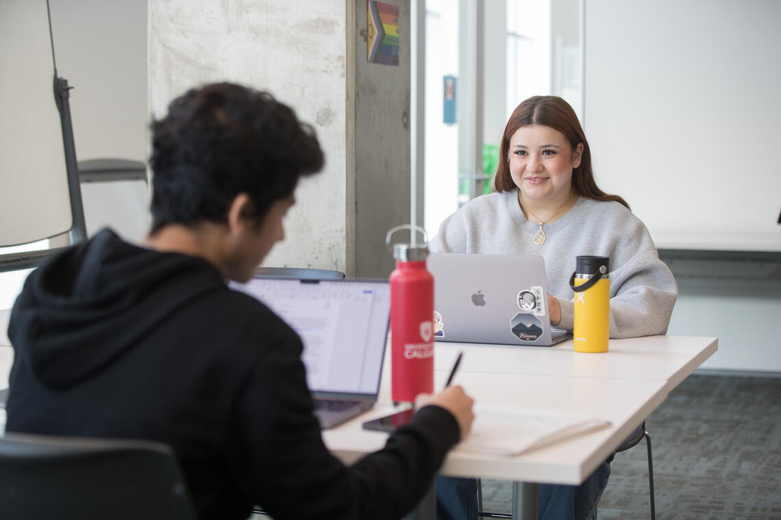 two students work together across the table from one another. 