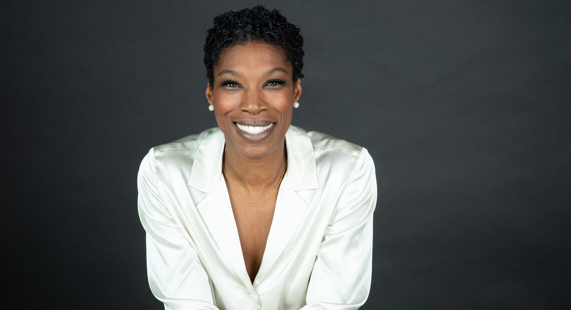 A woman with short dark hair wearing a white blouse smiles at the camera