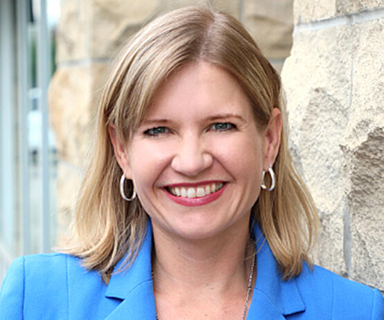 A woman with light hair and a blue blazer smiles at the camera