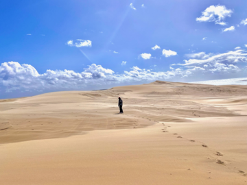 Person in the distance, walking across wide sandy dunes under a blue sky
