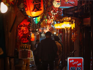 Looking down a dark, crowded alley lit by red lanterns