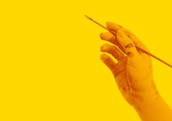 Hand holding a paintbrush against a yellow background