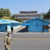 Looking across a concrete pad at a row of blue military houses, with a soldier on either side
