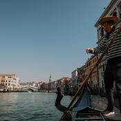 The photographer is seated in a low gondola, looking down a canal with the gondolier standing over them rowing