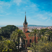 Looking down from above treetops towards a tall church steeple, with a broad city across the horizon in the background