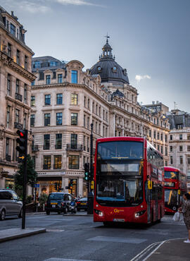 A red double-decker bus turns the corner, coming towards the photographer on a busy street