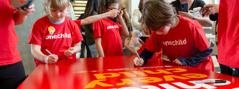 A group of kids in red t-shirts signing a large graphic board