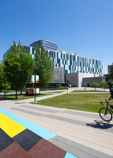 A student rides a bike on campus. The stairs of Mac Hall are visible and painted in rainbow colors.