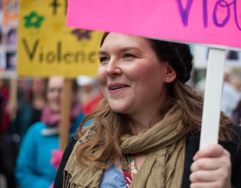 a woman with red hair carries a sign at a protest