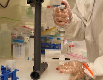 Close up of a woman using a pipette to pull white solution from a bottle.