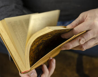 A man's hands are leafing through an open book. A hardcover book lies at his feet. Close-up, selective focus. Blur in motion.